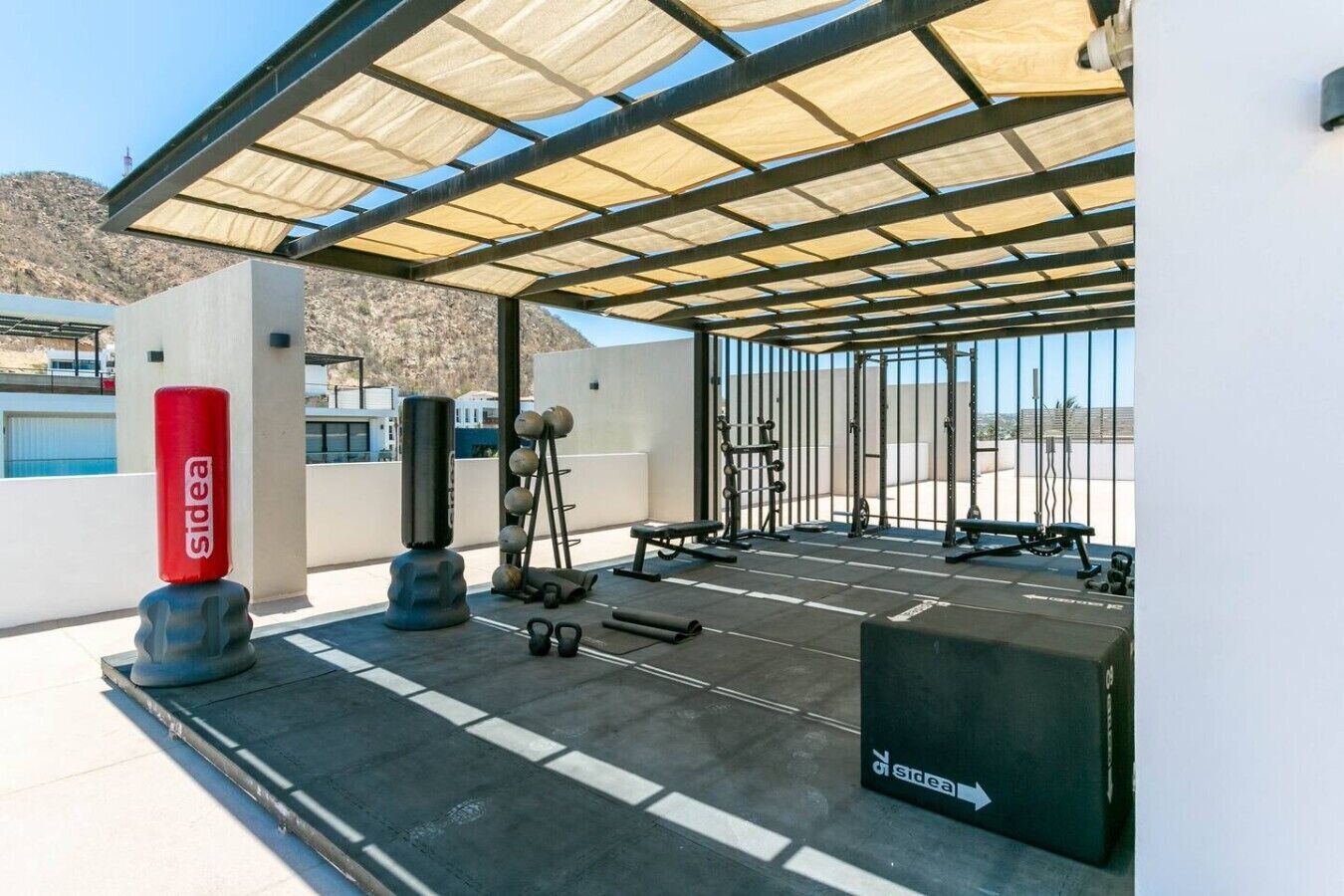 An outdoor gym area with exercise equipment, a shaded canopy, and a directional sign.