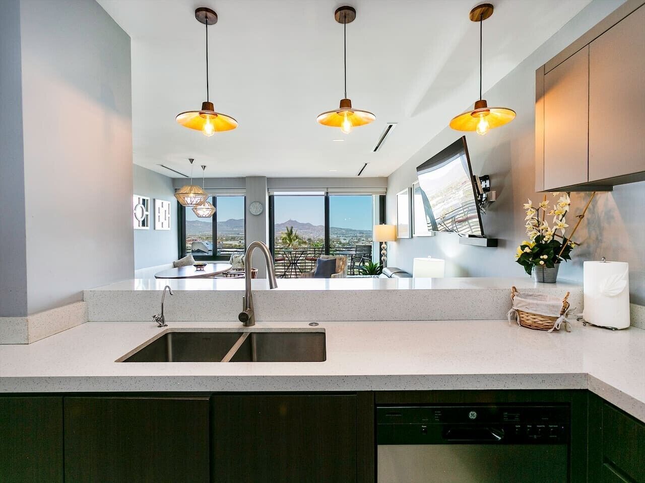A modern kitchen with a large island, stainless steel sink, and pendant lighting.