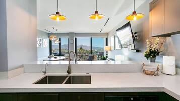 A modern kitchen with a large island, stainless steel sink, and pendant lighting.