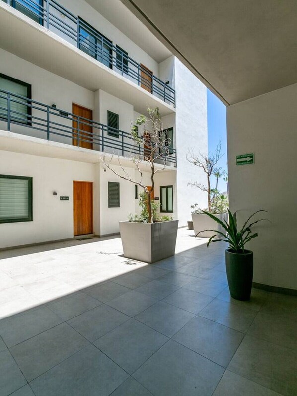 A modern building with a courtyard, featuring a large planter with a tree, a potted plant, and a sign indicating an exit.
