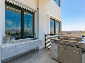 A balcony with a stainless steel grill, a built-in bench, and a view of the cityscape.