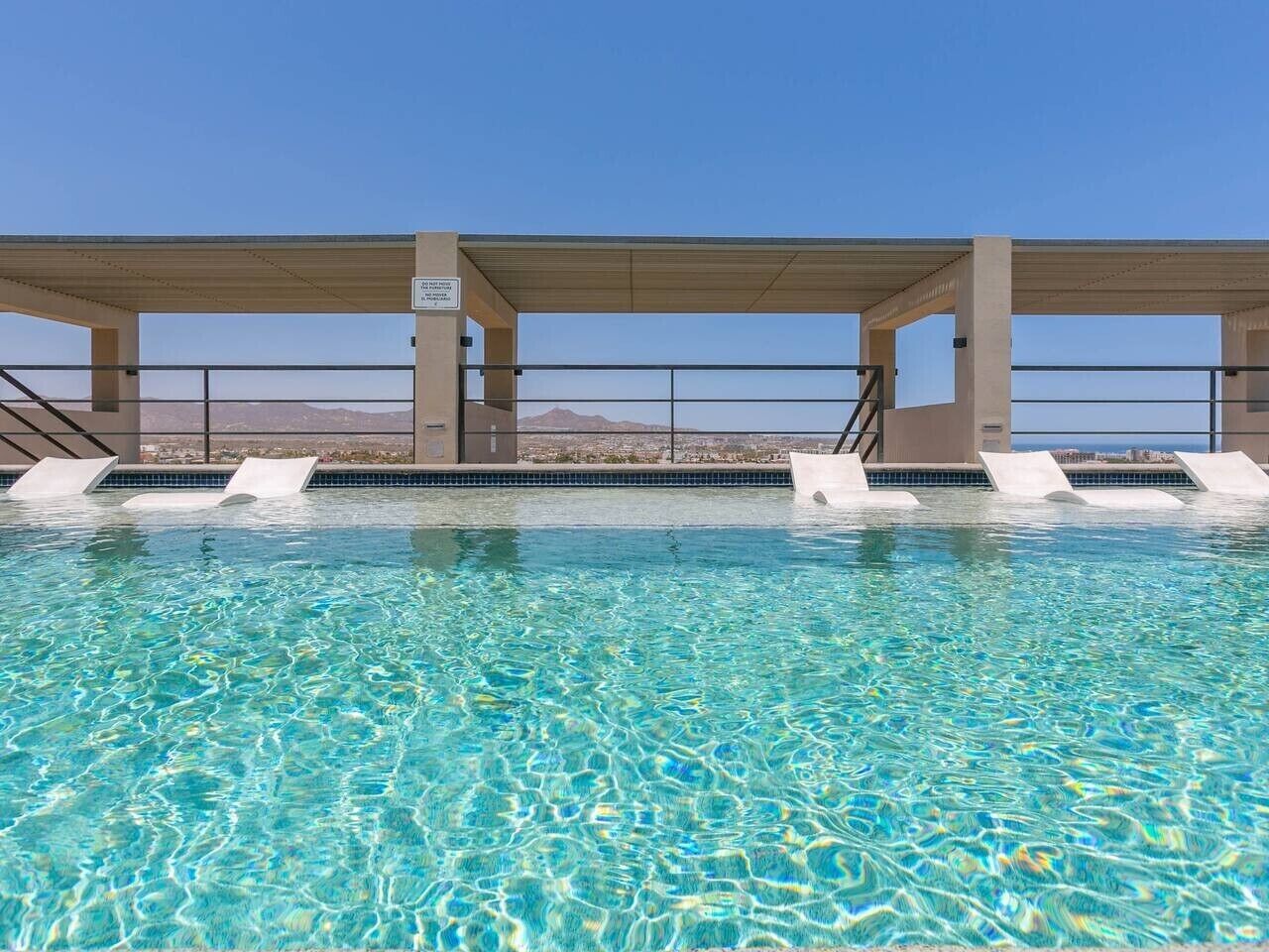 A swimming pool with clear water, surrounded by a covered area with steps leading down to the water.