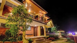 A two-story house with a balcony, a wooden door, and a well-lit garden area at night. - Blossom Stay (Mahabaleshwar)