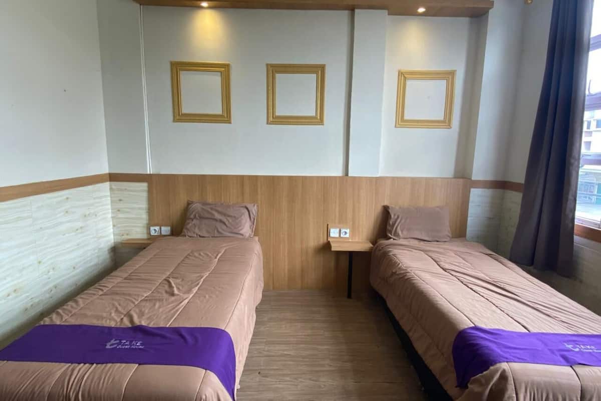A hotel room with two single beds, a wooden headboard, a small bedside table, and a window with curtains.