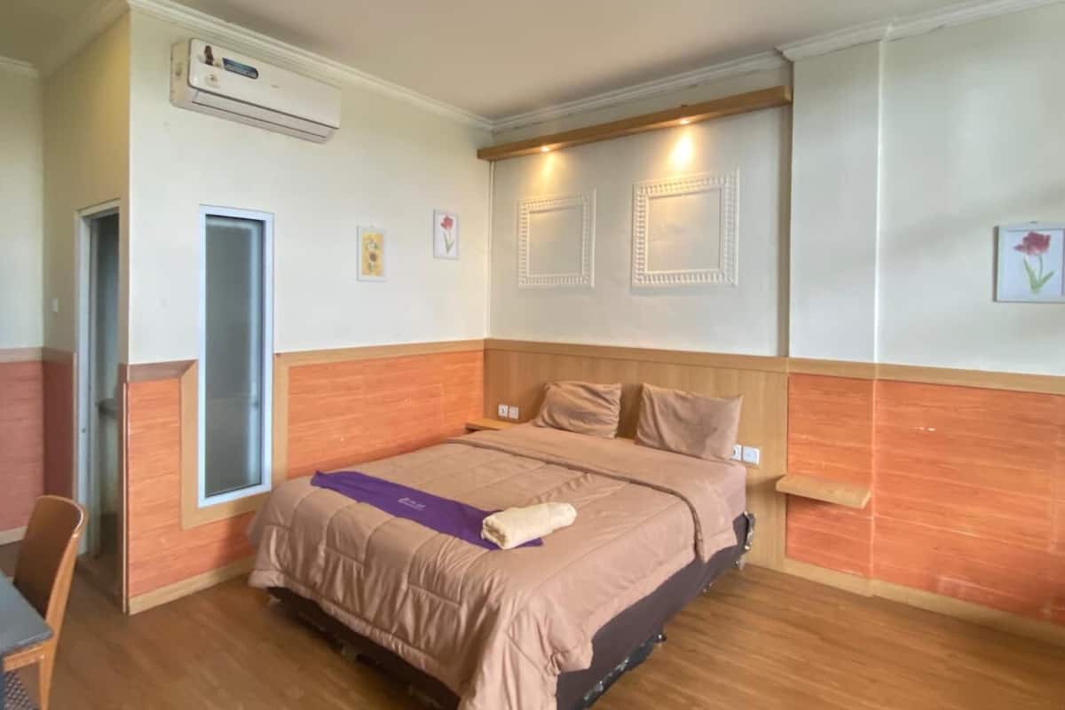 A hotel room with a bed, a desk, an air conditioning unit, and a door.