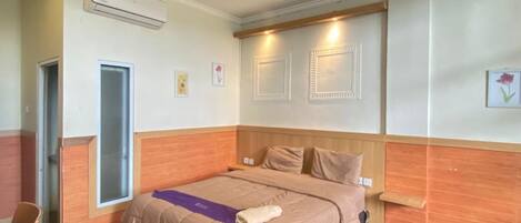 A hotel room with a bed, a desk, an air conditioning unit, and a door.