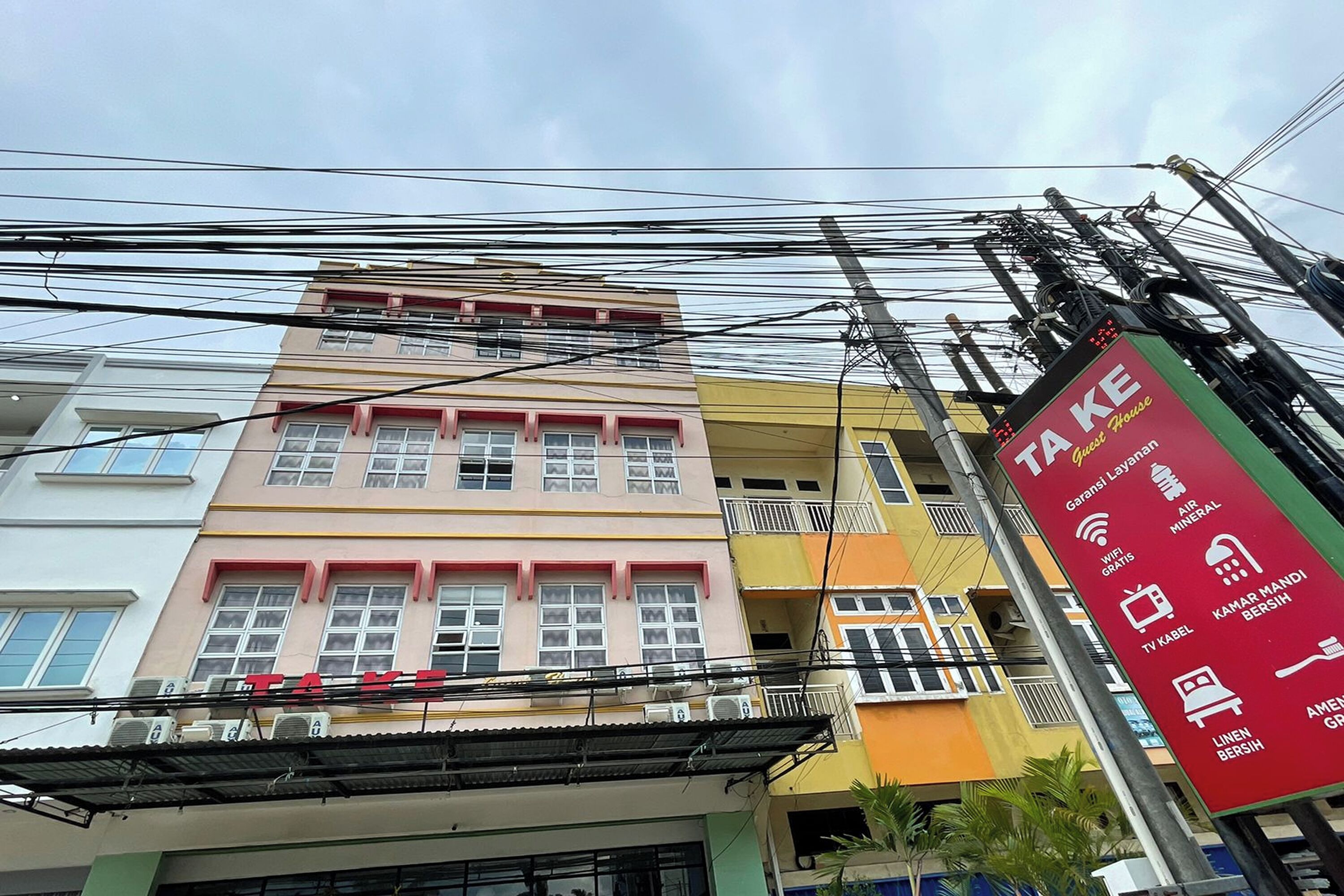 A multi-story building with a signboard listing amenities such as WiFi, air conditioning, and a TV.