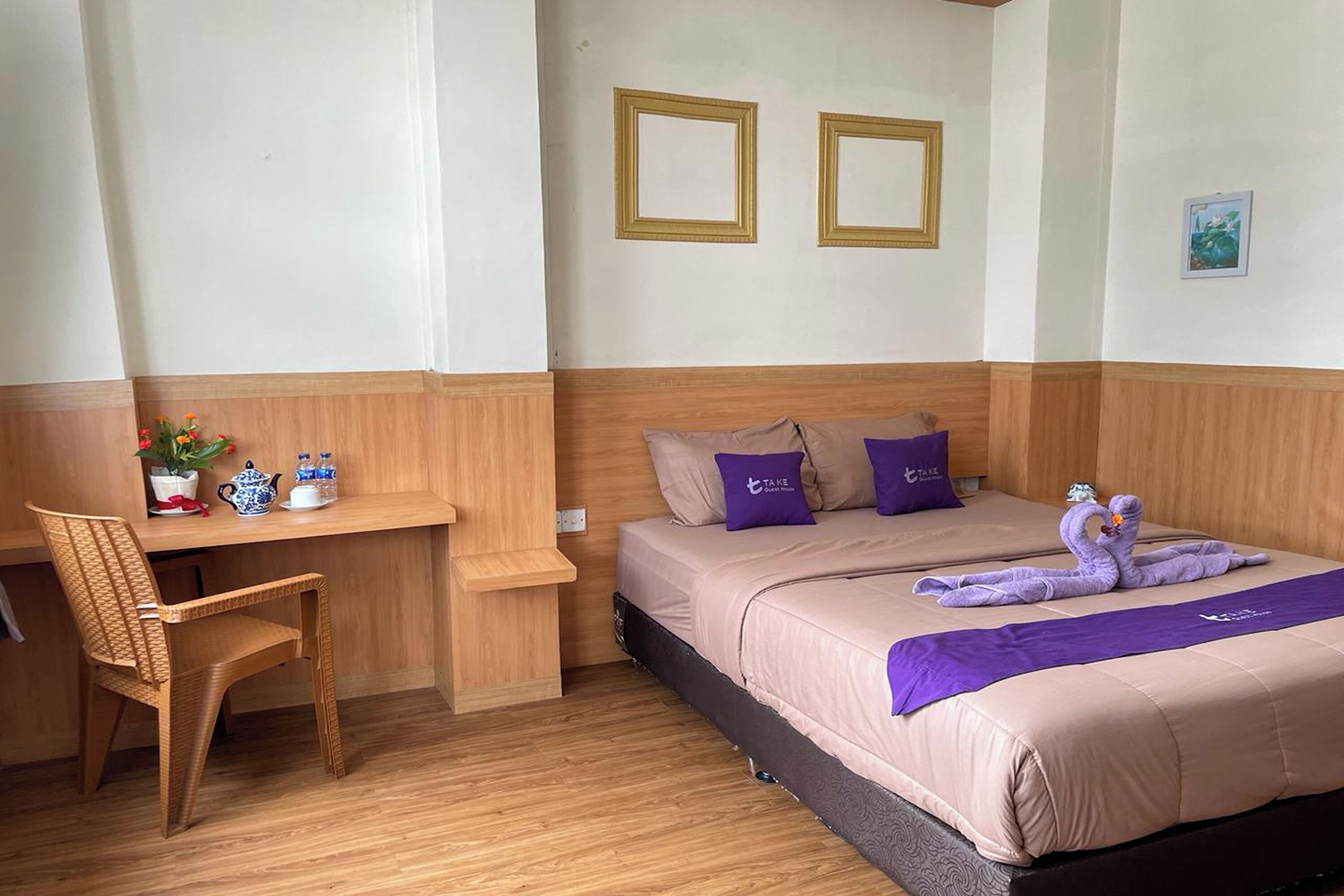 A hotel room with a bed, a desk, a chair, and a small table with a plant and a teapot.