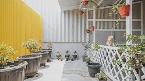 A courtyard with potted plants, a white fence, and a yellow wall. - Take Guesthouse 1 (Jambi)
