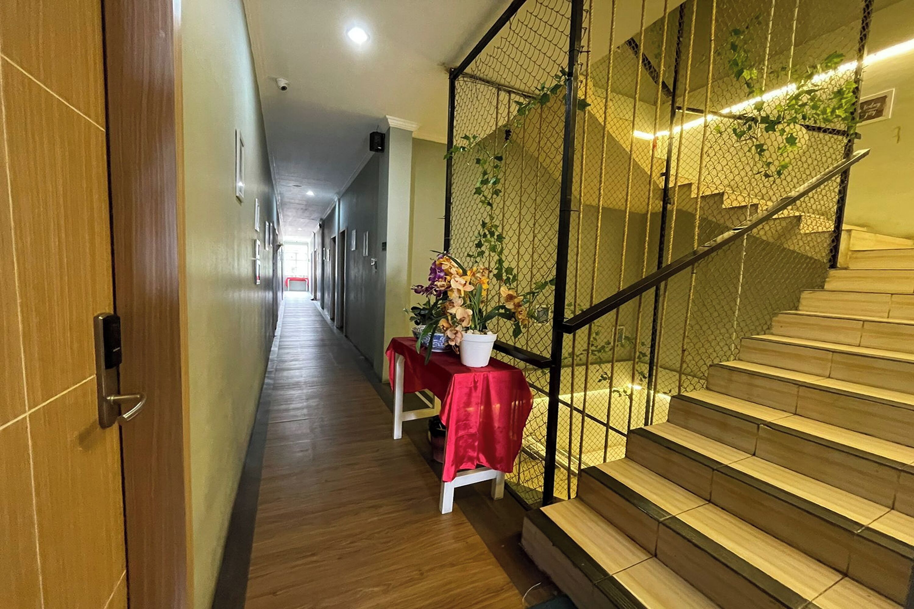 A hallway with a wooden floor, a red table with a potted plant, and a staircase with a metal railing.