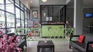 A modern hotel lobby with a green partition, seating area, and a bar counter. - Take Guesthouse 1 (Jambi)