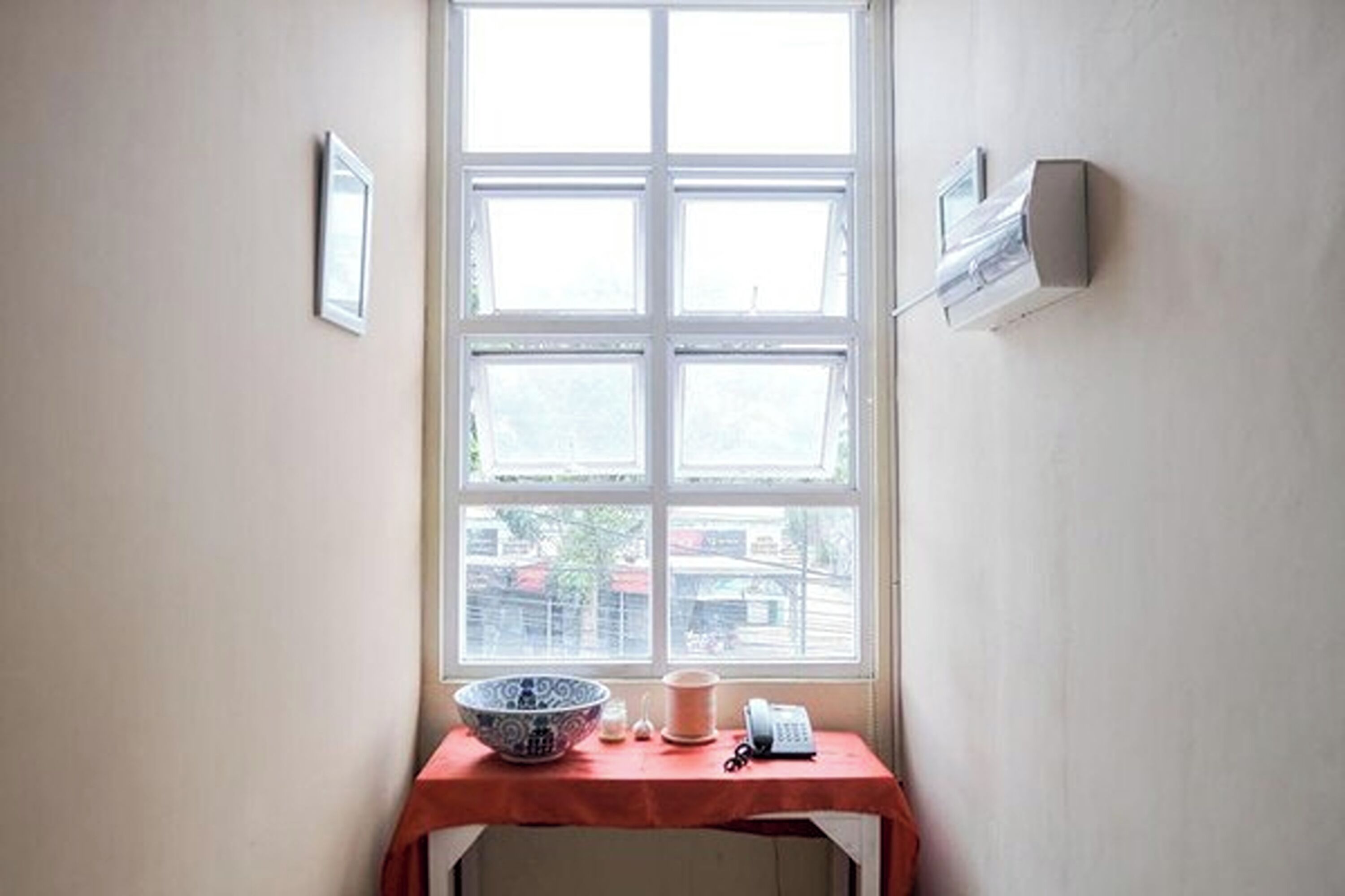 A room with a window, a table with a bowl, a cup, and a telephone.