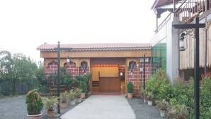 Un edificio con techo de tejas, entrada de madera y un pequeño jardín con plantas en macetas.