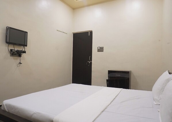 A hotel room with a bed, a television mounted on the wall, a door, and a small cabinet.