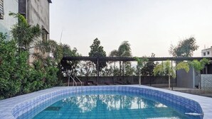 Una piscina con cubierta de baldosas, rodeada de vegetación y una pérgola.