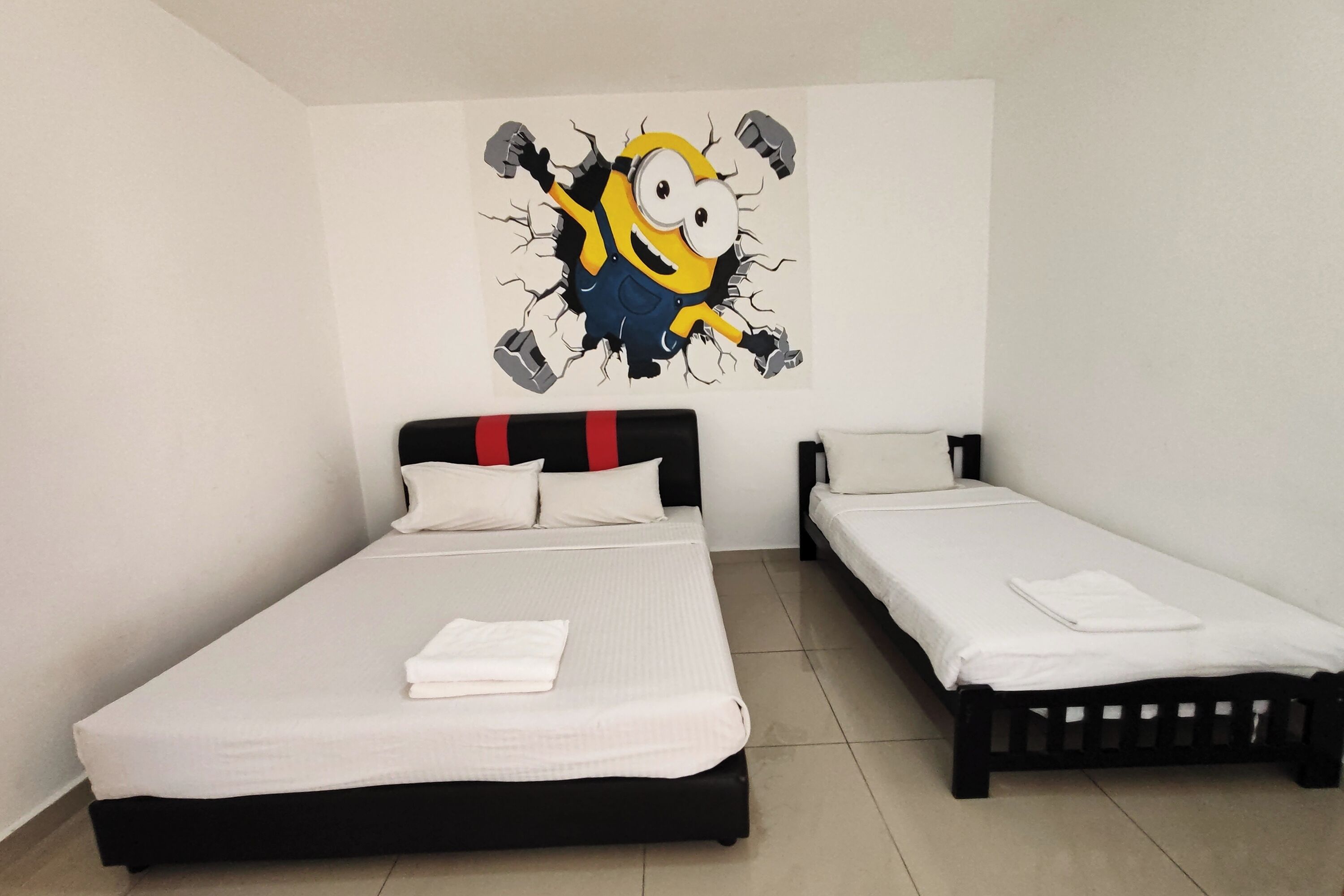 A hotel room with a large bed, a smaller bed, and a wall decoration of a cartoon character.