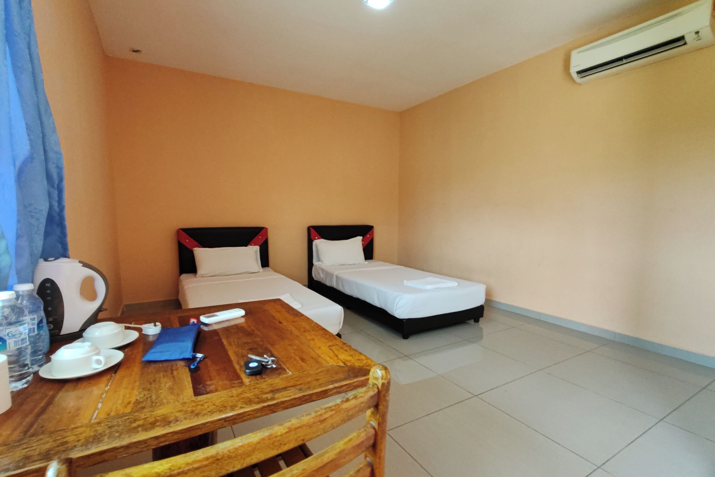 A hotel room with two single beds, a wooden table with a chair, a kettle, and a water bottle.