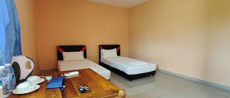 A hotel room with two single beds, a wooden table with a chair, a kettle, and a water bottle.