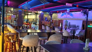 Zona de bar con mesas y sillas, un letrero de neón y un ventilador de techo.