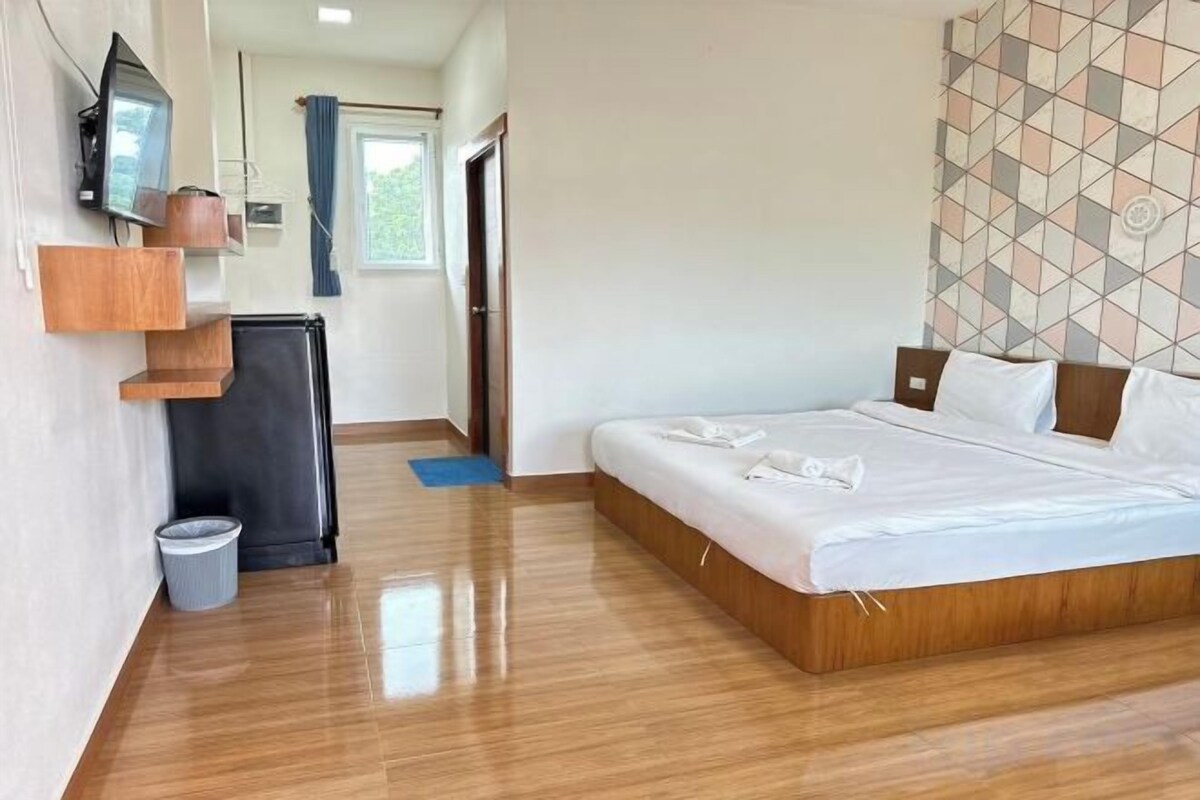 A hotel room with a bed, a TV, a small refrigerator, and a trash bin.