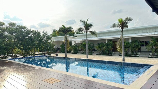 A swimming pool with a tiled deck, surrounded by palm trees and a building with a white roof. - The White House P&N Hotel Chiang Rai (Wiang Chai)