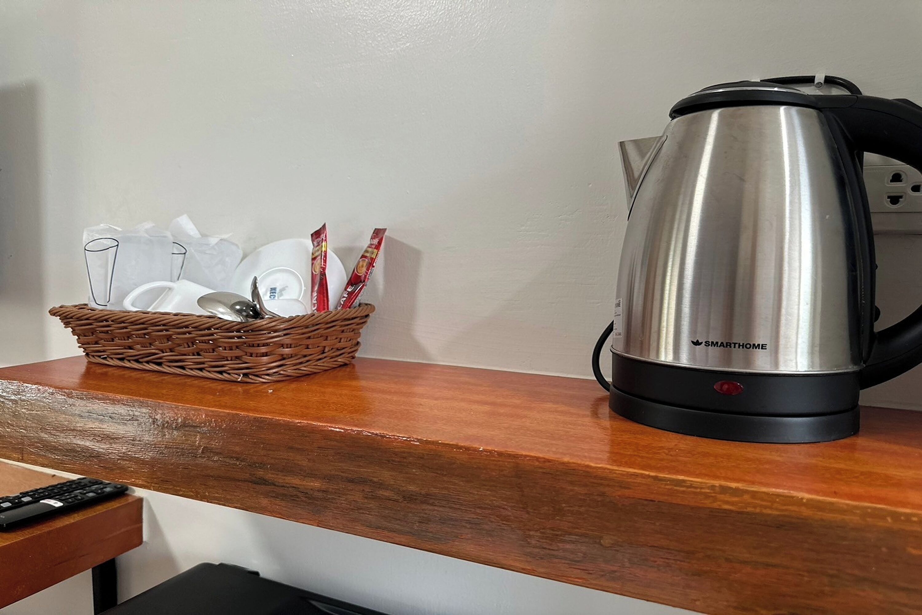 Un comptoir de cuisine avec une bouilloire électrique en acier inoxydable et un panier en osier contenant des tasses et des ustensiles.