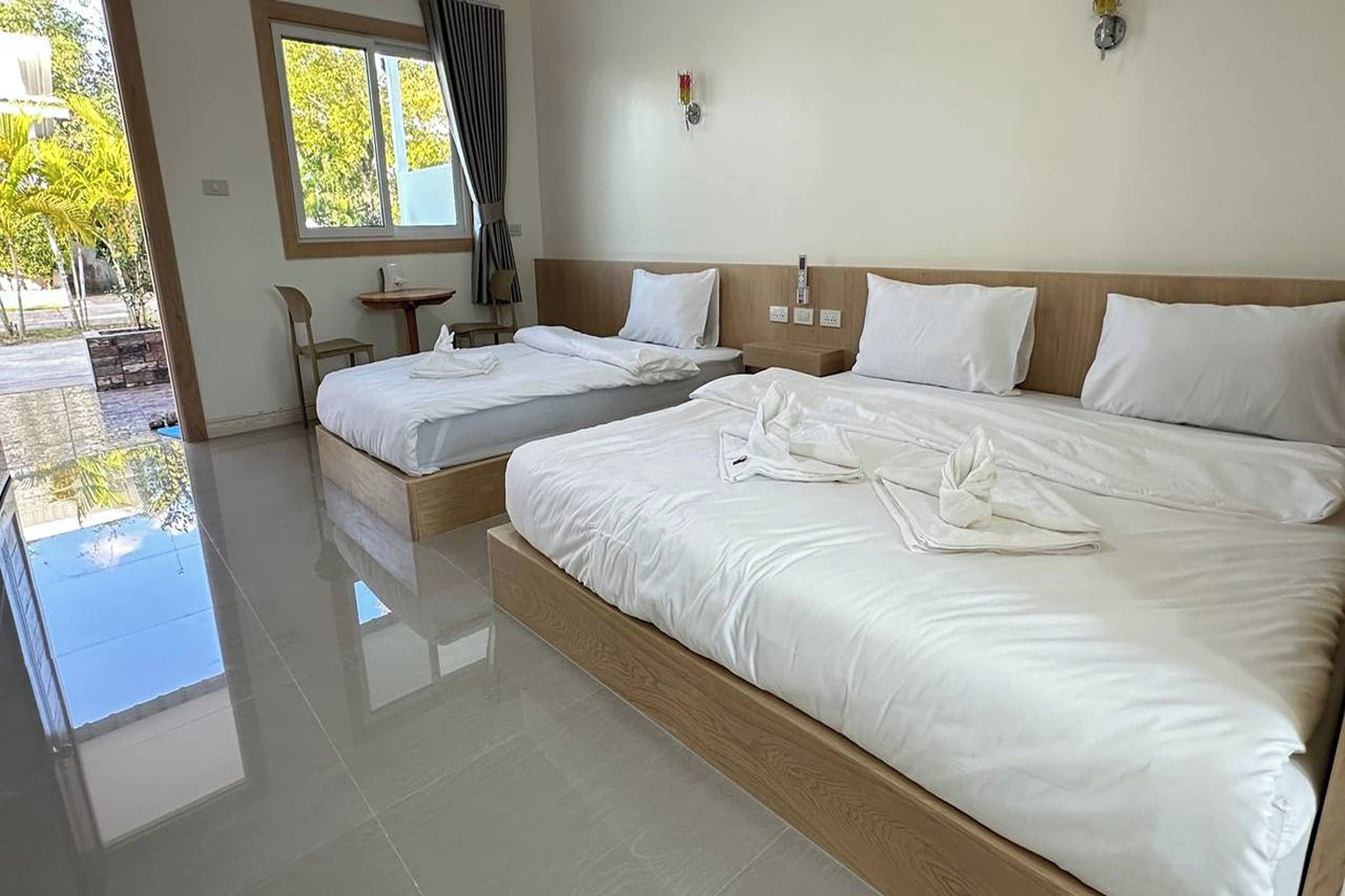 A hotel room with two beds, a small table, and a window with curtains.