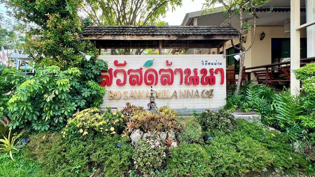 A signboard with Thai text and a small statue in front of a building with a tiled roof. - Sawadeelanna Hotel (Nan)