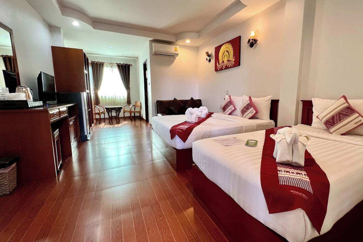 A hotel room with two beds, a desk with a television, and a dining area.