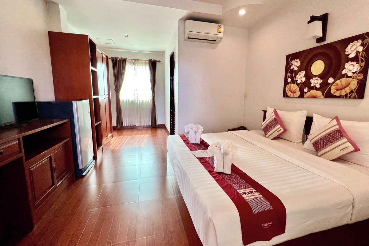 A hotel room with a bed, a TV, a wardrobe, and a painting on the wall.