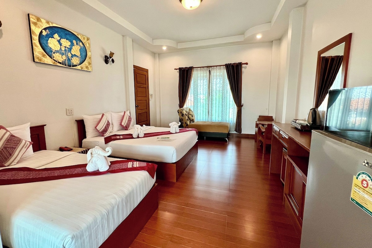 A hotel room with two beds, a desk, a television, and a large window with curtains.