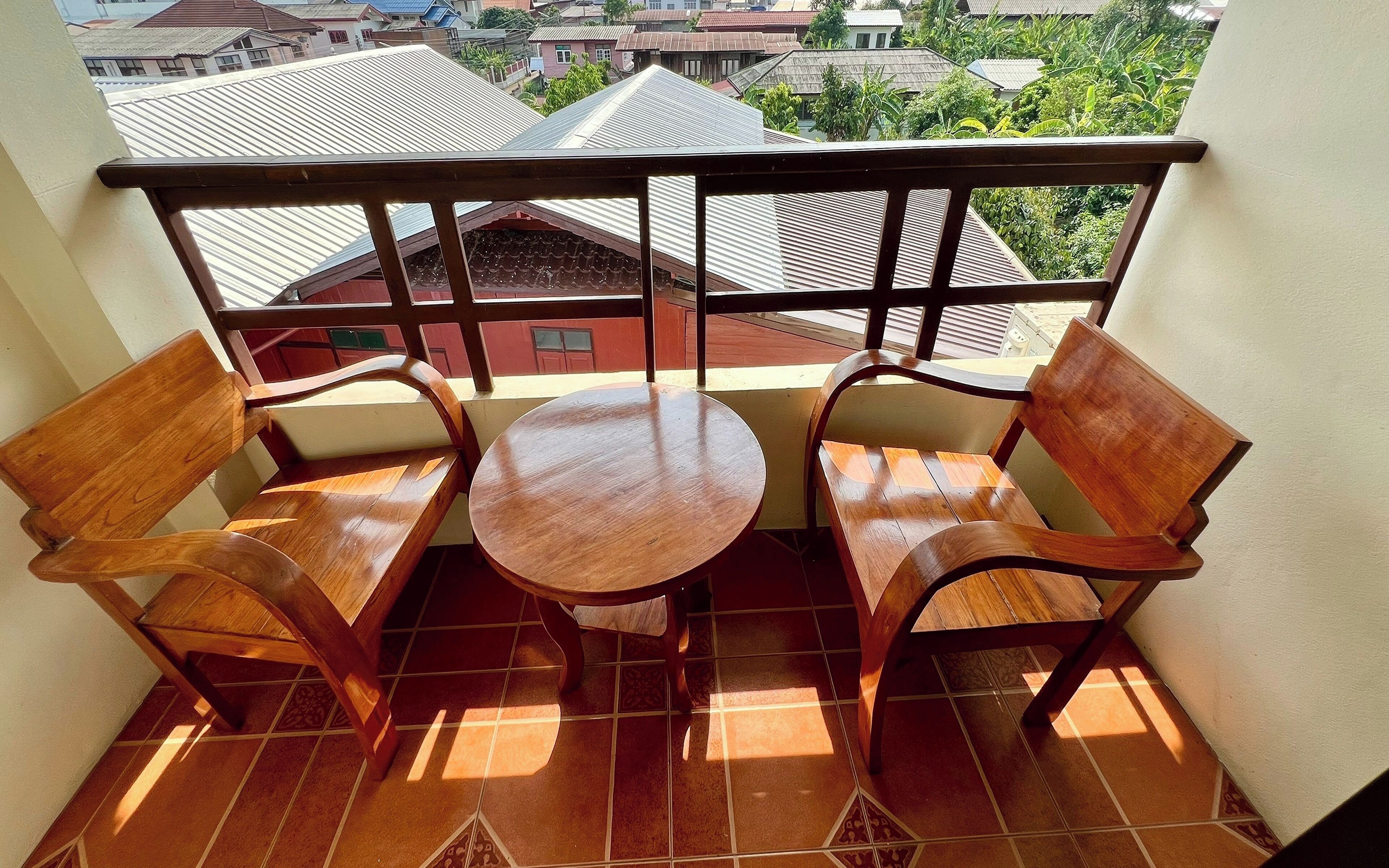 A balcony with two wooden chairs and a small round table, overlooking a residential area with houses and greenery.
