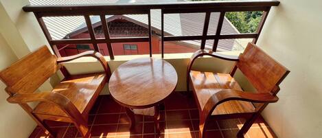 A balcony with two wooden chairs and a small round table, overlooking a residential area with houses and greenery.