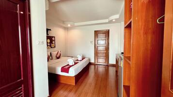 Quarto de hotel com piso de madeira, cama com roupa de cama branca e detalhe vermelho, guarda-roupa de madeira e porta que dá para outro quarto.