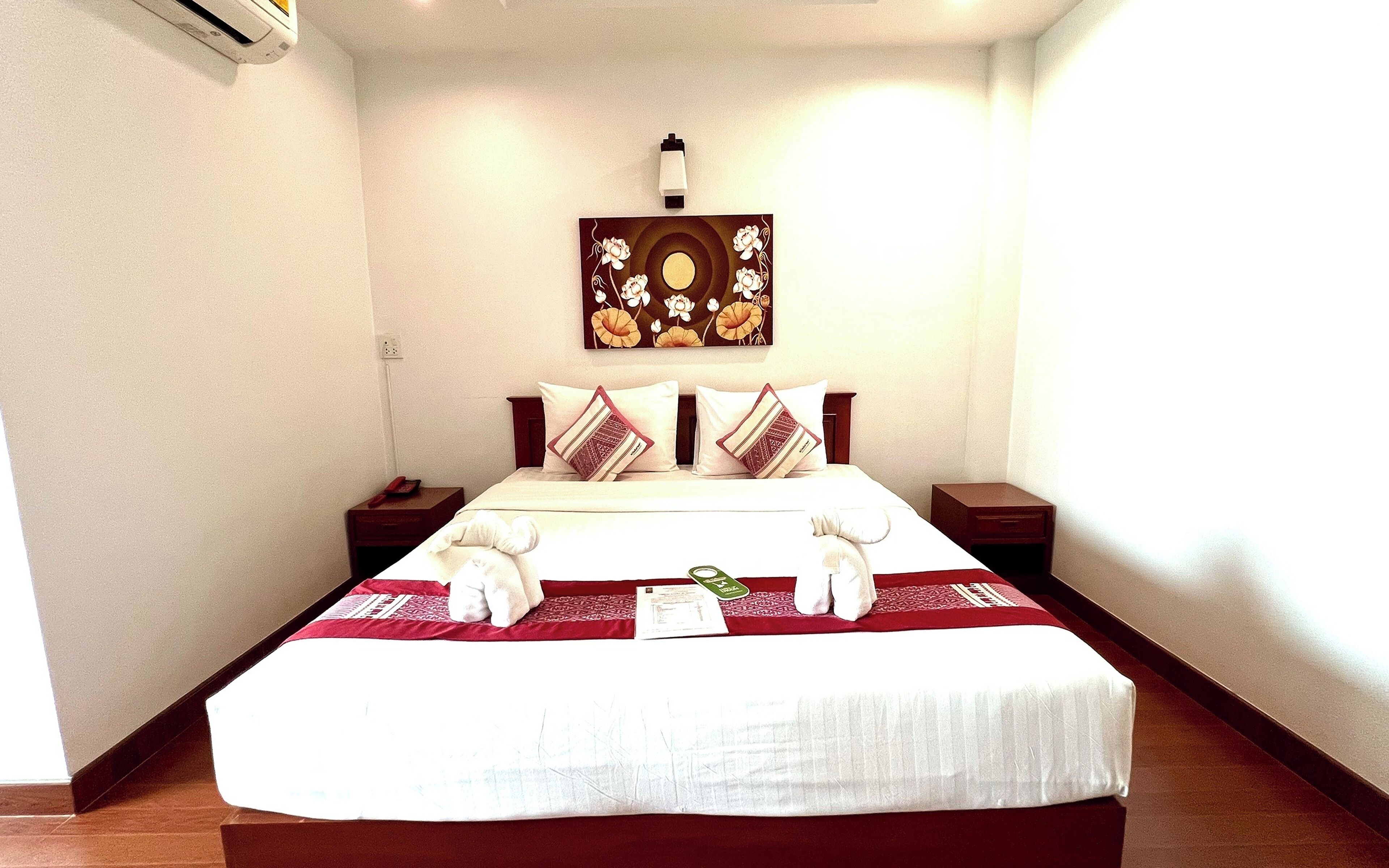 A hotel room with a large bed, a nightstand, a bedside table, a wall-mounted light, and a painting above the bed.