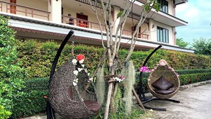 A garden with two wicker swings, a tree, and a building in the background. - Sawadeelanna Hotel (Nan)