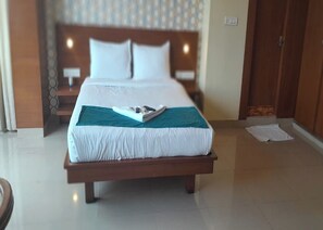 A neatly made bed with a teal throw, a wooden headboard, and a nightstand with a lamp. - Fortune Suites (Bengaluru)