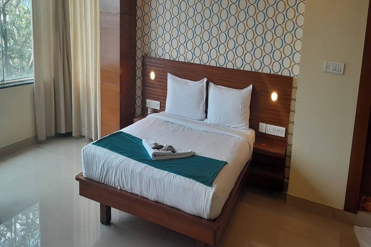 A hotel room with a wooden bed, white bedding, a teal throw blanket, and a patterned wall.