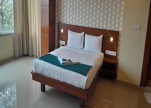 Ein Hotelzimmer mit einem hölzernen Bett, weißer Bettwäsche, einer türkisblauen Tagesdecke und einer Wand mit Muster.