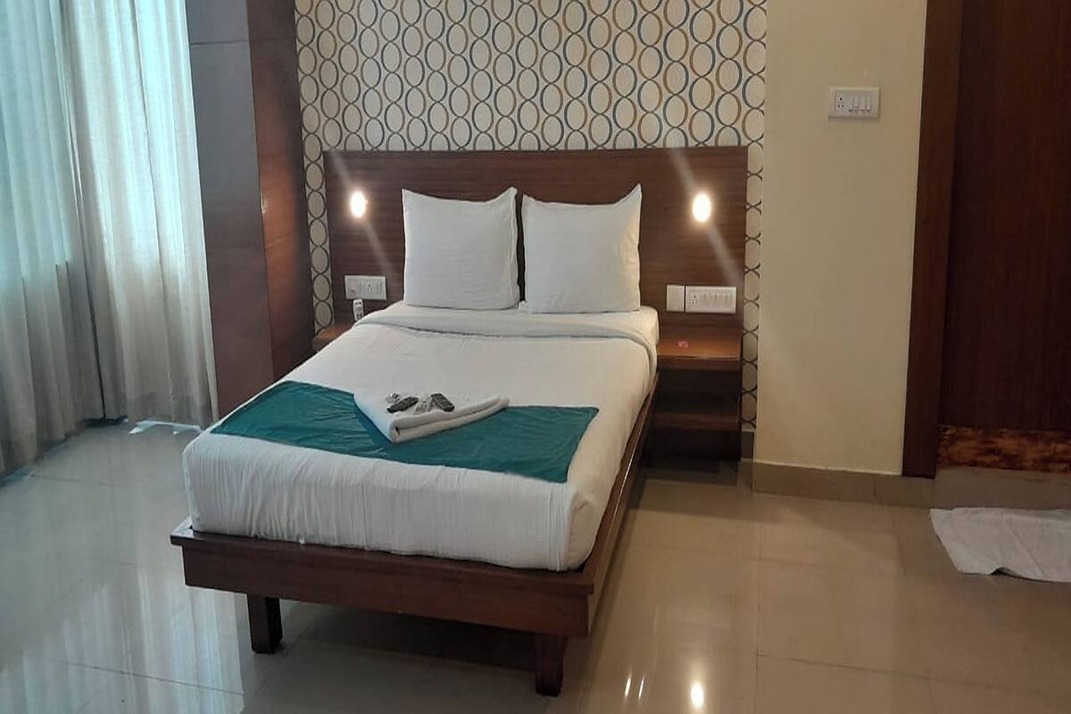 A neatly made bed with white linens and a teal throw blanket, a wooden headboard, and a patterned wall in the background.