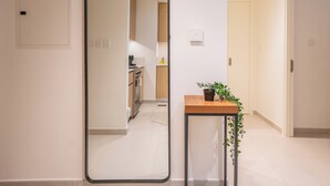A modern kitchen with a stove, oven, and coffee maker. There is a wooden side table with a plant and a mirror on the wall.