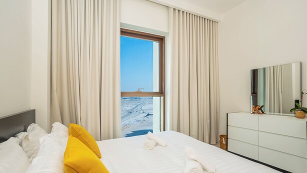 A hotel room with a bed, a dresser, a mirror, and a window with a view of the beach.