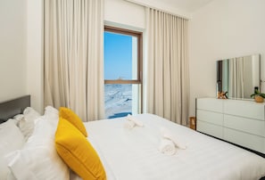A hotel room with a bed, a dresser, a mirror, and a window with a view of the beach.