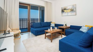 A modern living room with a blue sofa set, a wooden coffee table, and a large window with a view of the city.