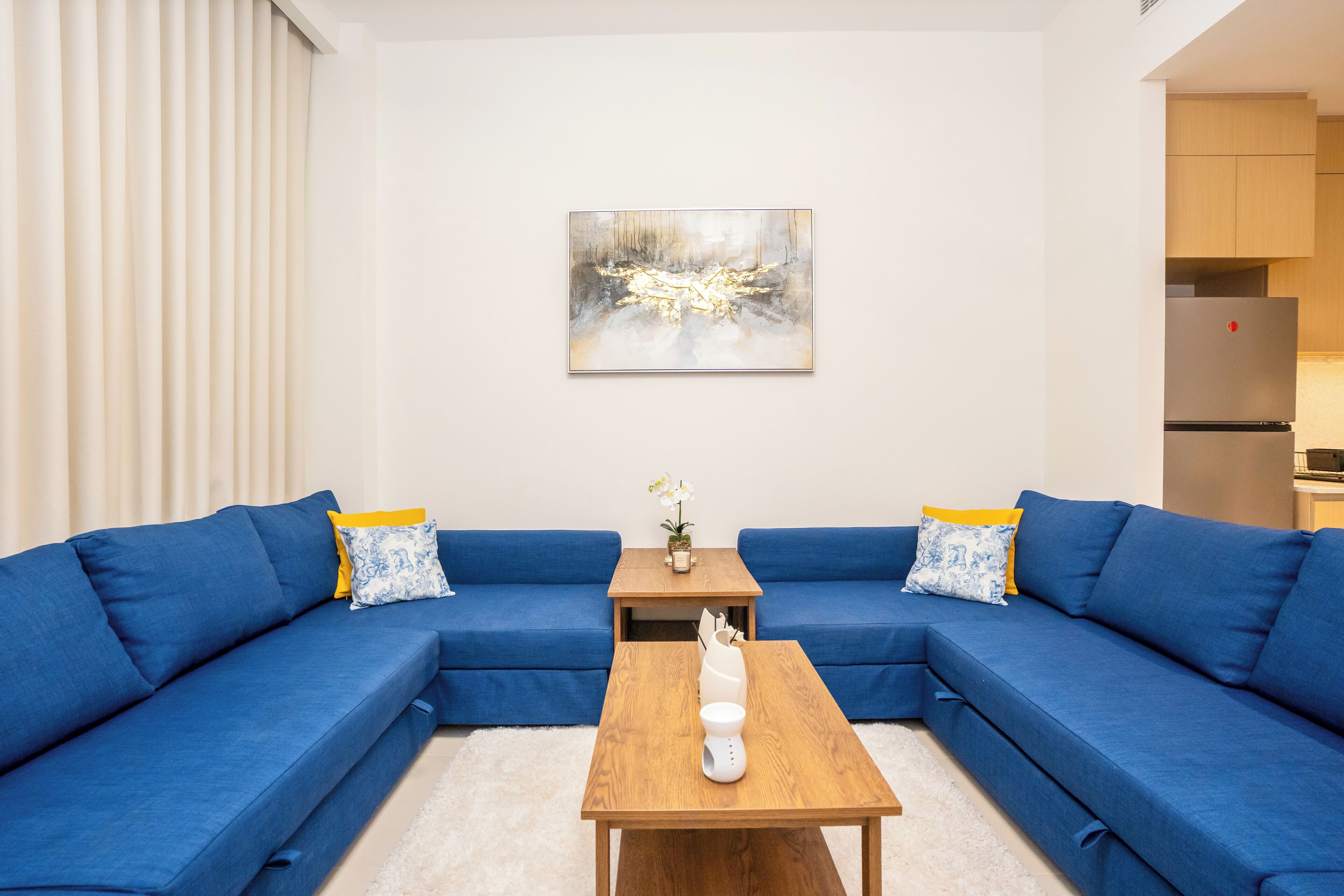 Un salon moderne avec un canapé d’angle bleu, une table basse en bois et un tableau accroché au mur.