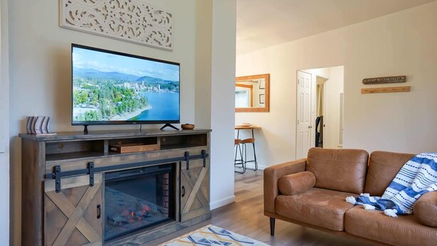 Una sala de estar con chimenea, televisor, sofá de cuero marrón y alfombra estampada.