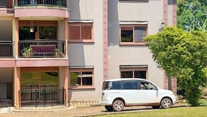 Un immeuble résidentiel à plusieurs étages, doté de balcons, avec une voiture blanche garée devant.