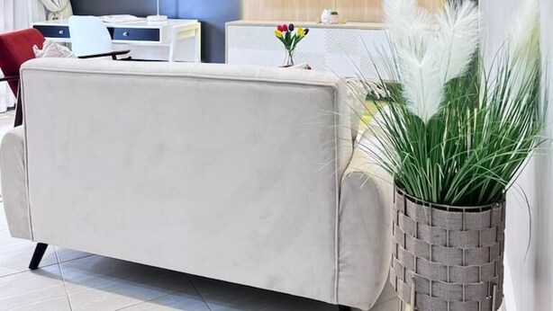 Un salon moderne comprenant un canapé, un téléviseur à écran plat fixé sur un panneau en bois, un bureau avec une lampe et une œuvre d’art encadrée accrochée au mur.