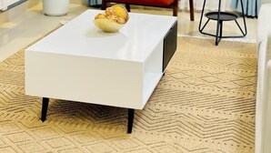 Un salon moderne avec une table basse blanche, un fauteuil rouge agrémenté d’un coussin à motifs, une plante en pot et une petite table ronde sur laquelle est posée une plante.