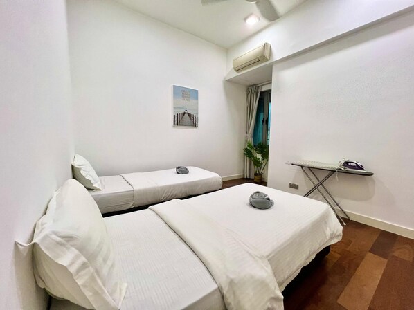 A small, clean room with two single beds, a small table with an iron, and a potted plant. - Capital O 90987 The Loft Residences Homestay @ Imago Shopping Mall 2 (Kota Kinabalu)